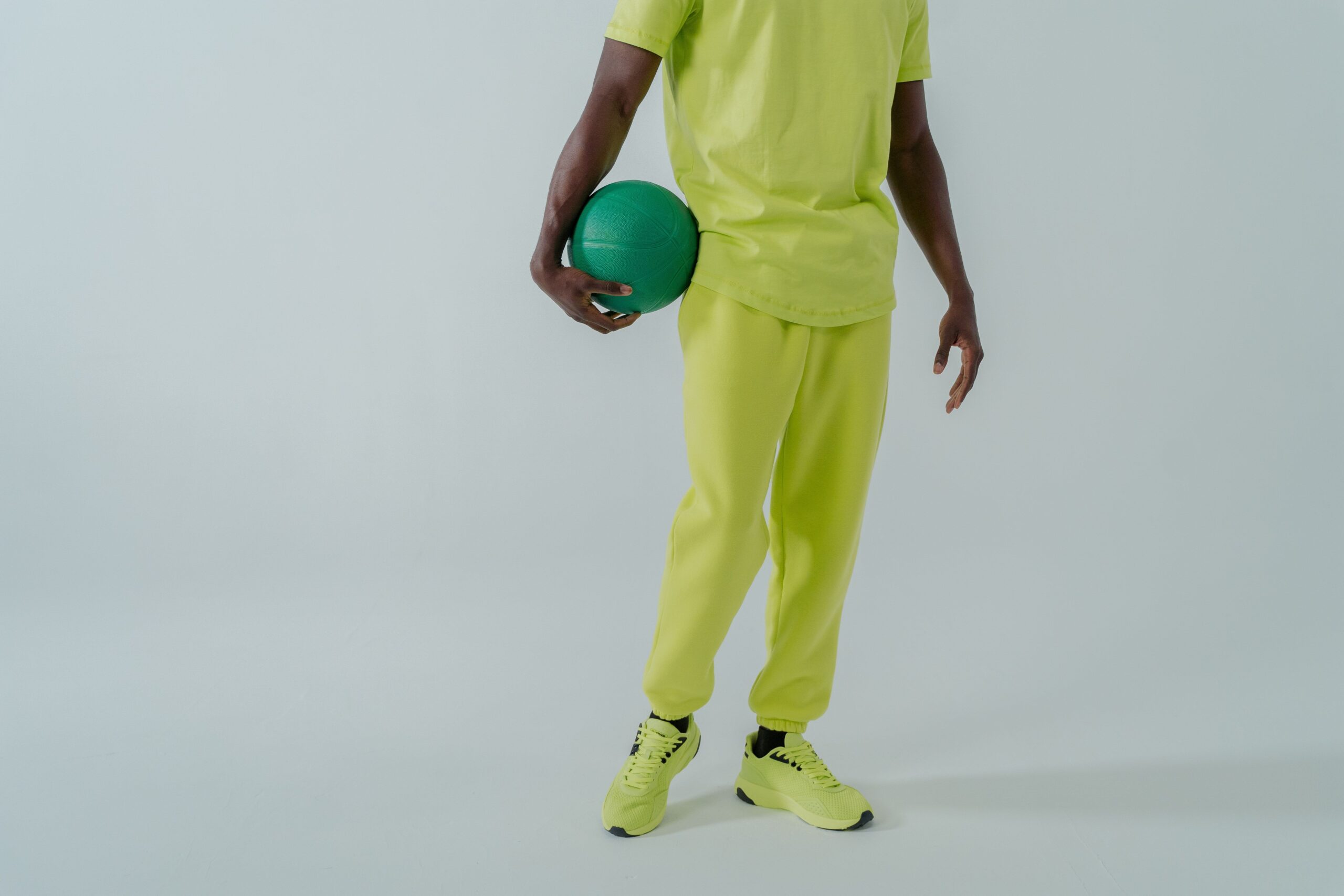 Stylish man in a lime green tracksuit holding a ball in a studio setting.